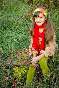 绿草背景下，手里拿着玫瑰果丛的秋装女孩
