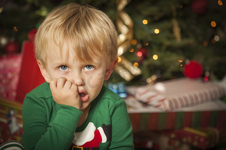 脾气暴躁的小男孩坐在圣诞树旁