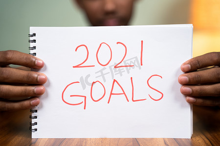 新年目标摄影照片_桌上的男人在镜头前拿着 2021 年目标书 — 规划 2021 年新年目标的概念。