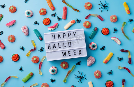 蓝色背景上放着万圣节节日装饰品和糖果，灯箱上写着 Happy Halloween flat