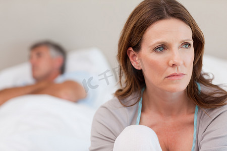 年代感卧室摄影照片_悲伤的女人躺在床上，背景是她的丈夫