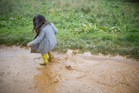 快乐的小女孩在泥泞的水坑里快乐地跳跃和飞溅