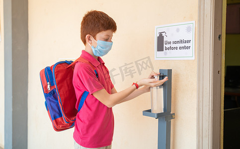 带医用口罩的孩子在进入教室前使用洗手液 — 返校或学校重新开放的概念以及冠状病毒或 covid-19 安全措施。