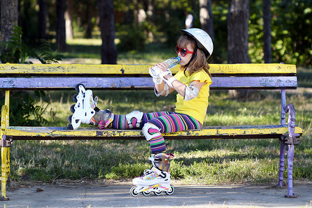 穿旱冰鞋的小女孩坐在长凳上喝水