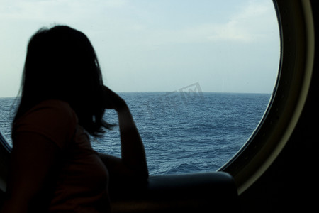 一个女孩透过游轮的舱口望向大海