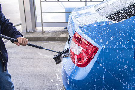 在阳光明媚的夏日，用刷子在洗车设施上洗车。在外面的洗车场用加压水手动洗车。在外面的洗车场用加压水手动洗车。