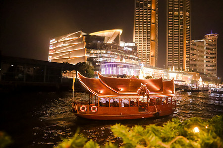 泰国夜景摄影照片_曼谷夜景和一艘在河中航行的游船。