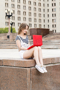 年轻漂亮的女人带着笔记本电脑坐在大学附近的楼梯上