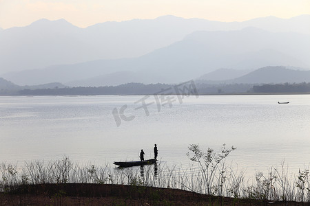 黄昏湖边摄影照片_渔夫在湖边的木船上的轮廓。