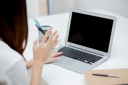 年轻的亚洲女商人使用笔记本电脑空白屏幕模型进行在线视频通话，并在家中交流工作、带笔记本的女孩会议、社交距离、沟通理念。