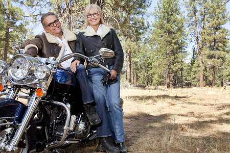 靠着树木摄影照片_老年夫妇在森林里靠在摩托车上
