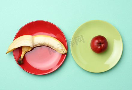 瓷碟摄影照片_红熟的苹果和香蕉放在一个圆形的陶瓷盘子里