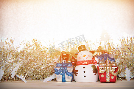 金色飘带摄影照片_可爱的雪人、圣诞礼盒或礼物，以及木头、银色闪光背景上的金色飘带或金属丝