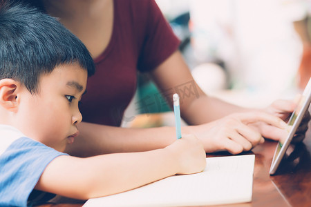 学习在线摄影照片_儿子使用数字平板电脑学习和学习与母亲一起在线上网、家庭教育、家庭娱乐、妈妈教男孩和家庭作业与技术、生活方式概念。