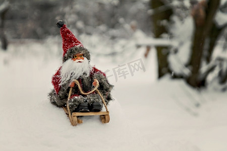 白雪皑皑的森林摄影照片_玩具圣诞老人在白雪皑皑的森林里的雪橇上