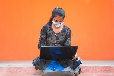 戴着医用面具的年轻女学生忙于在 caollege 走廊或大学校园的笔记本电脑上工作 — 大学重新开放的概念，由于冠状病毒或 covid-19 大流行而成为新常态。