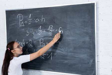 一个十几岁的女孩正在用白色粉笔在学校黑板上写字来解决学校的数学问题。