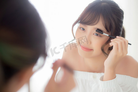 女性眉毛摄影照片_美丽的年轻亚洲女人化妆眉毛刷，男朋友