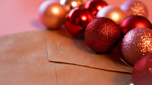 粉红色背景上带有圣诞红和粉红色球的牛皮纸信封