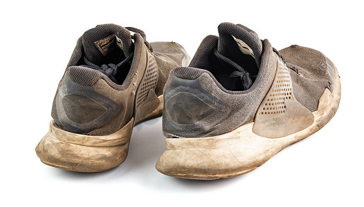 运动鞋摄影照片_一双白色背景中突显的破旧脏运动鞋
