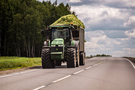 俄罗斯图拉 — 2019 年 7 月 30 日：在夏季道路上滚动的拖车中装有绿色青贮饲料的拖拉机