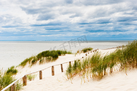 海边漂流摄影照片_在沙丘的篱芭在有可见的风雨如磐的云彩的海边。