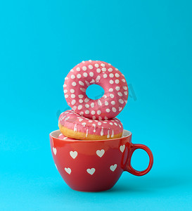 蓝色背景中红色陶瓷杯中的一堆粉红色甜甜圈，上面有糖霜