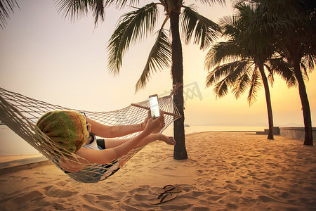 pho摄影照片_女人躺在沙滩摇篮里用 smart pho 拍照