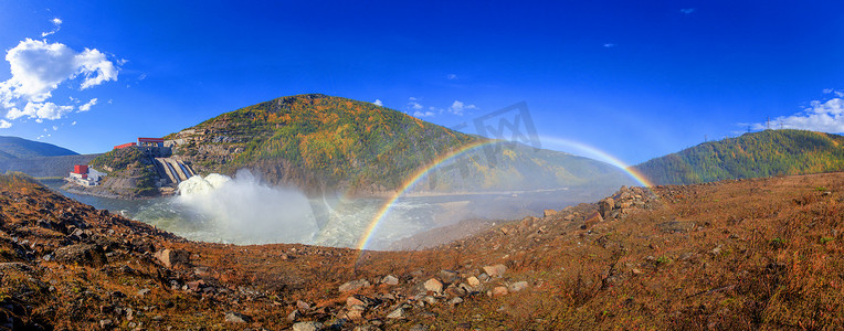 全尺寸美丽明亮的彩虹以秋天的山丘和一条小溪为背景。