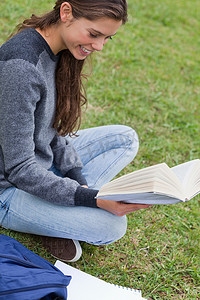 年轻微笑的女人盘腿坐着拿着一本书