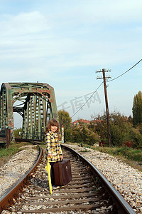 带雨伞和手提箱的小女孩在铁路上