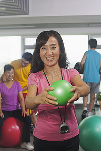 前景是拿着球的女人，背景是在健身房锻炼的人