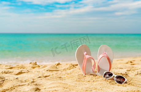 粉色和白色凉鞋，海边沙滩上的太阳镜。 