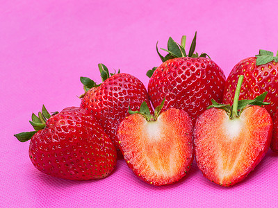 草莓丁摄影照片_表面布满种子的草莓甜红果粉红色织物上红莓心形水果的特写质地