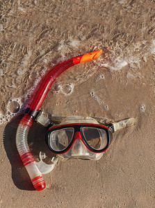 面具和通气管躺在潮湿的沙滩上，有波浪