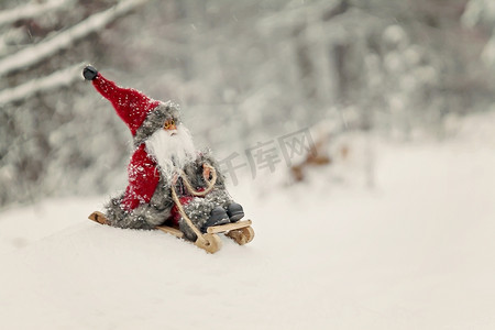 玩具圣诞老人在白雪皑皑的森林里的雪橇上