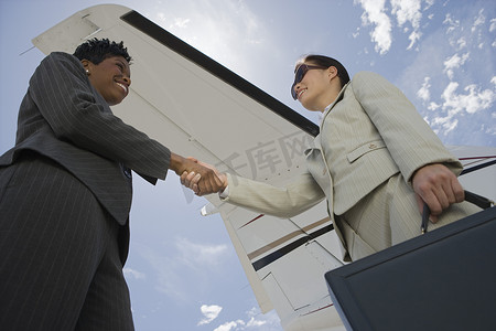 两位女商人与飞机机翼握手的低视角