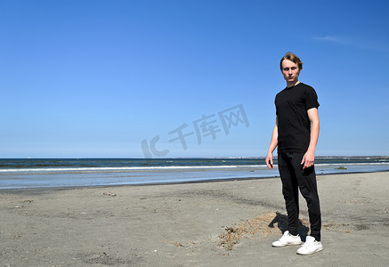 黑t恤的人摄影照片_黑衣服和白色鞋子的年轻男性站立在海滩