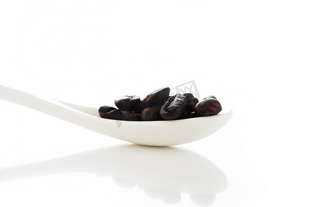 白色背景中带浅色参考的白色勺子中的咖啡豆