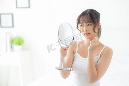 美丽的亚洲年轻女性照镜子，脸上有粉刺问题