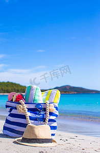 白色沙滩上的蓝色包、草帽、人字拖和毛巾