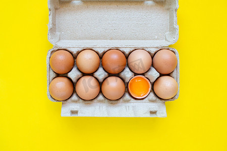 特写镜头在黄色背景上并排放置的纸盒中破裂了棕色鸡蛋和鸡蛋。