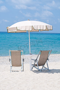 沙滩上的两把躺椅在伞下