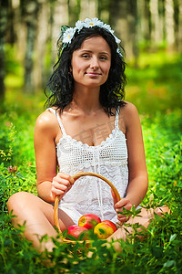 美丽的女孩坐在草地上，拿着一篮子苹果