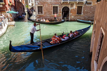 意大利，威尼斯 - 2012 年 7 月：2012 年 7 月 16 日在威尼斯，游客在一条小运河上巡航的长平底船交通繁忙。