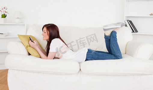 美丽的红发女性在躺着的时候在手机上写短信