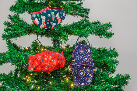 绿树枝条摄影照片_圣诞 covid-19 面具挂在一棵带灯的绿树上作为装饰。