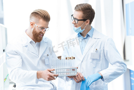 穿着白大褂的年轻微笑男化学家在实验室拿着试管