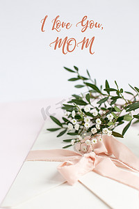 白色粉色背景的信封，上面有桃色丝带、绿枝和鲜花。