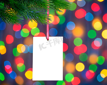 节日灯光背景下冷杉枝上的圣诞贺卡